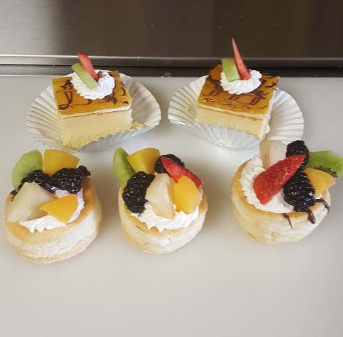 Two fruit-topped pastries and two square desserts with cream and fruit, arranged on a white surface.