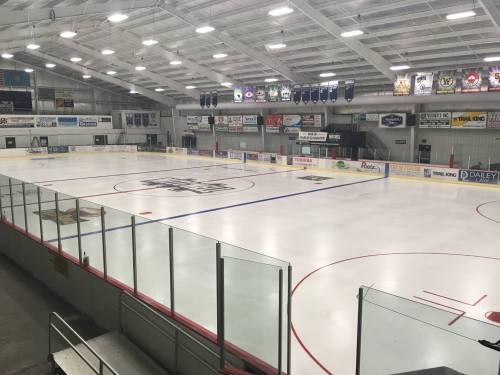 Empty ice rink with red and blue lines, surrounded by glass barriers and banners hanging from the ceiling.