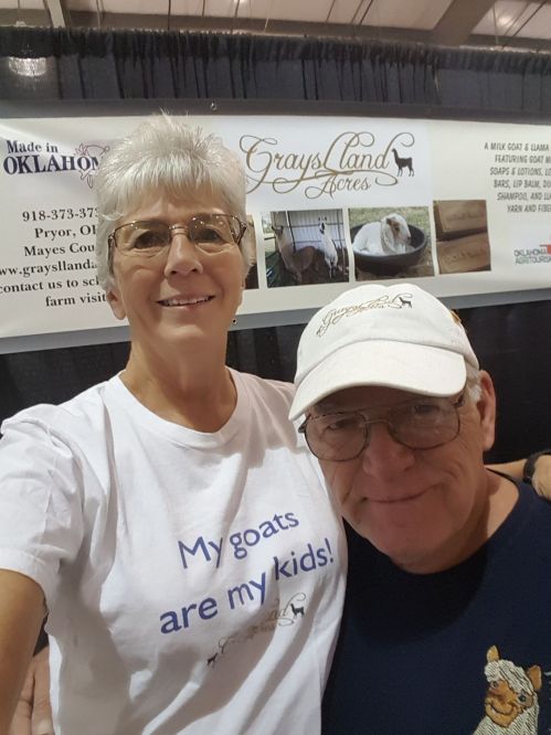 A smiling woman in a white shirt and a man in a cap pose together at a booth for Graysland Farm.