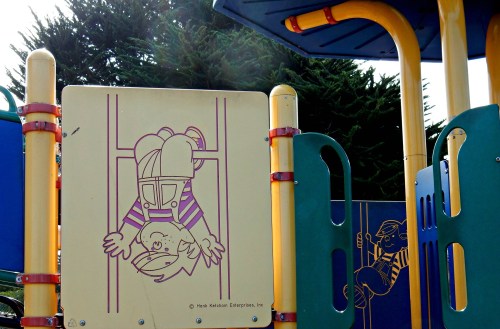 Playground equipment featuring a colorful panel with cartoon children playing, one hanging upside down.