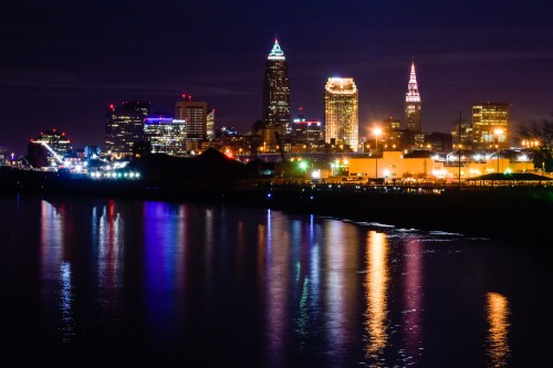 Cleveland skyline at night, featuring illuminated buildings reflecting on the water.