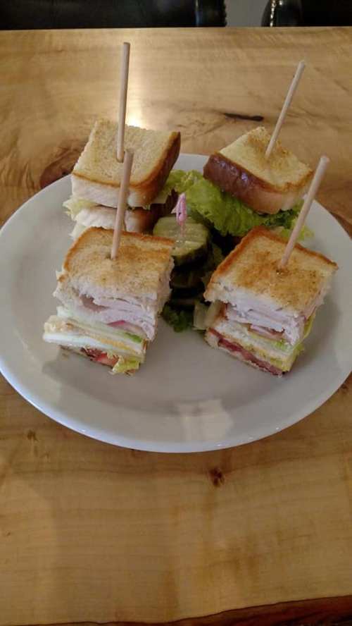 A plate with four stacked sandwiches, each held together with a toothpick, surrounded by lettuce and pickles.