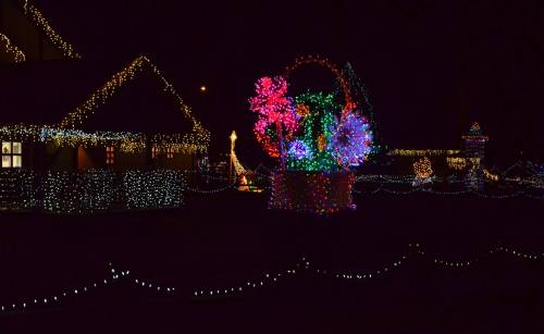 A festive display of colorful lights and decorations illuminating a house and garden at night.