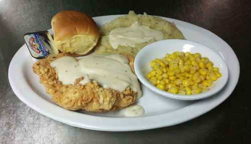 A plate with fried chicken topped with gravy, mashed potatoes, corn, a roll, and a butter packet.