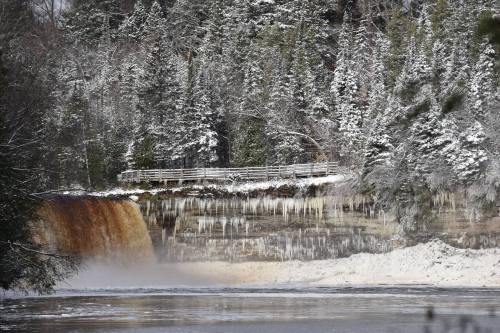 A snowy landscape featuring a waterfall surrounded by evergreen trees and ice formations.