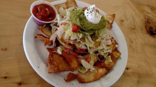 A plate of nachos topped with lettuce, guacamole, salsa, and a dollop of sour cream, served with a side of salsa.
