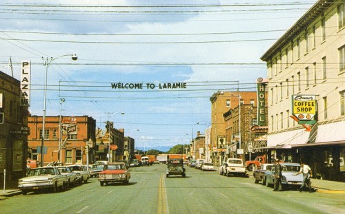 A historic street view of Laramie, featuring shops, cars, and a "Welcome to Laramie" sign overhead.