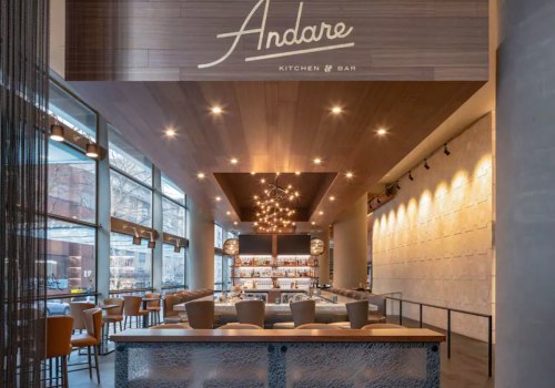 Modern restaurant interior featuring a bar, stylish seating, and warm lighting with "Andare Kitchen & Bar" sign.