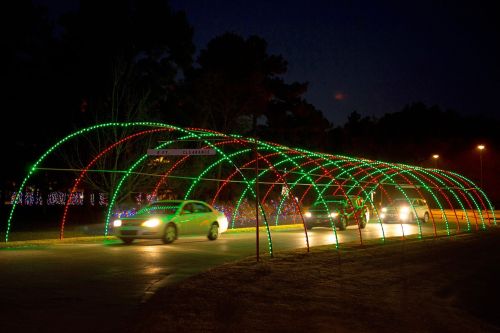 Cars drive through a colorful light tunnel decorated with red and green lights at night.