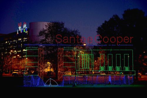 Colorful holiday lights spell out "Santee Cooper" against a twilight sky, with festive decorations in the background.