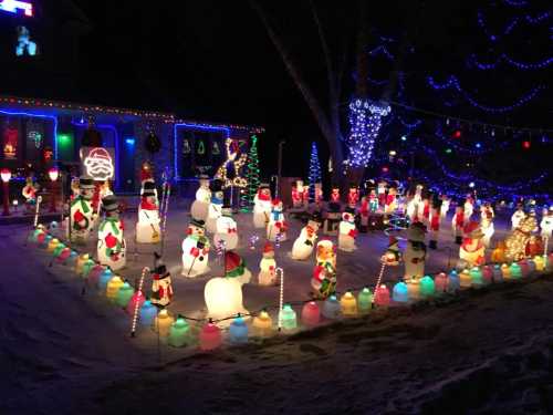 A festive outdoor display featuring numerous illuminated snowmen and colorful lights in a snowy yard.