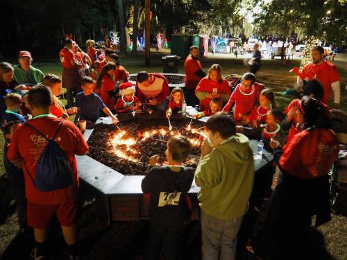 A festive gathering around a fire pit, with children and adults roasting marshmallows and enjoying holiday lights.