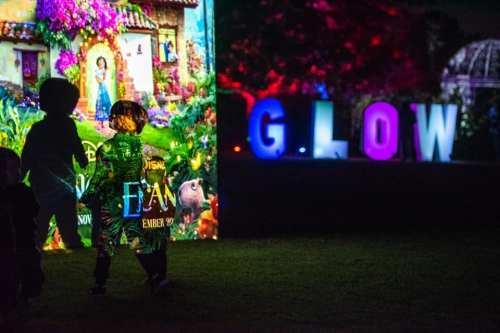 Children play in front of a colorful projection and illuminated letters spelling "GLOW" at an outdoor event.