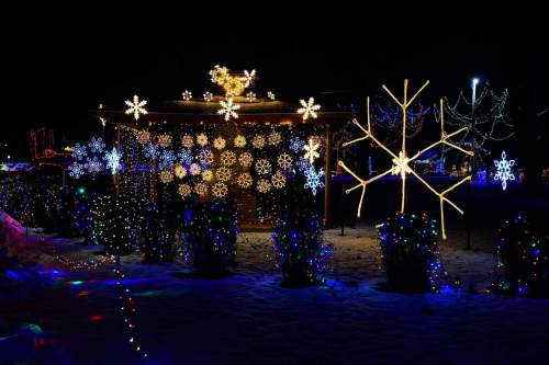 A festive display of colorful Christmas lights, featuring snowflakes and a reindeer, set against a snowy night backdrop.