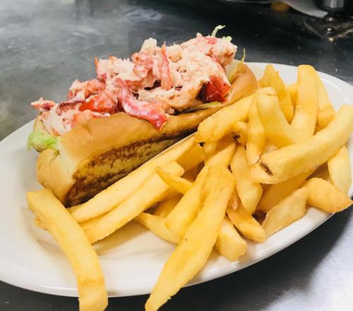 A lobster roll topped with lobster meat on a bun, served with a side of golden French fries.