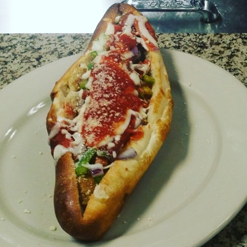A large, stuffed sandwich on a plate, filled with vegetables, sauce, and topped with cheese.