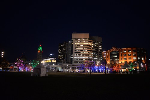 City skyline at night, featuring colorful holiday lights on trees and buildings.