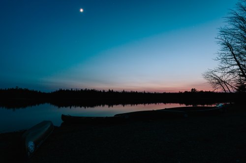 A serene lake at dusk, with canoes on the shore and a gradient sky transitioning from blue to pink.