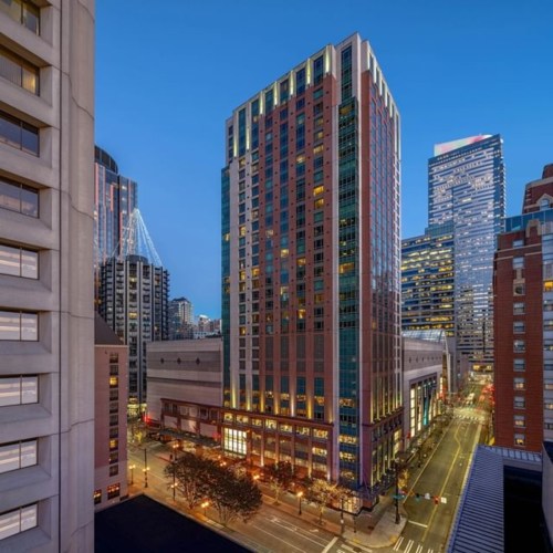 City skyline at dusk, featuring tall buildings and illuminated streets in an urban setting.