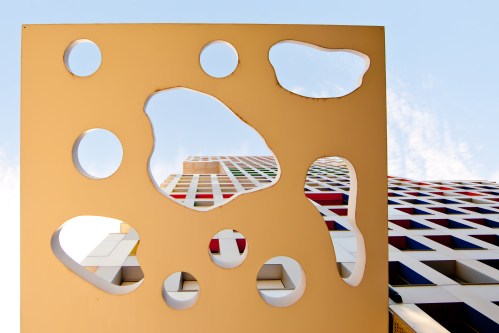 Abstract architectural design featuring a colorful building viewed through a cut-out panel with various shapes.
