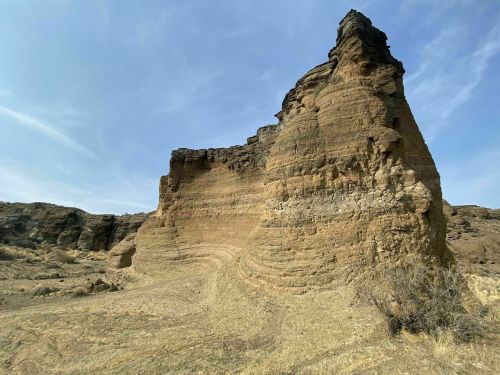 A rugged rock formation with layered textures rises against a clear blue sky in a dry landscape.
