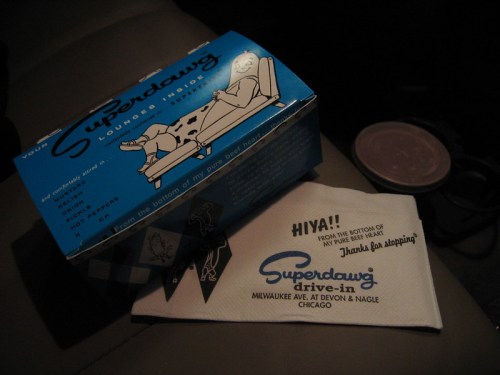 A blue takeout box from Superdawg Drive-In with a napkin featuring the restaurant's logo and a friendly message.