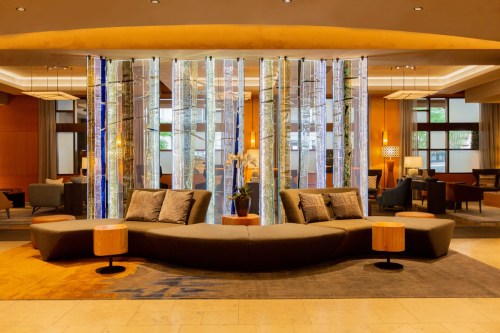 Modern hotel lobby featuring a curved sofa, wooden tables, and decorative glass panels in a stylish, inviting space.