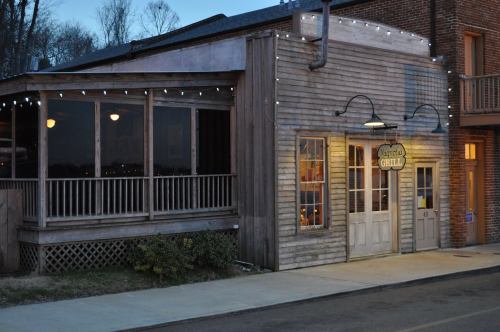 A rustic wooden building with string lights, featuring a sign that reads "Grill," set against a twilight sky.