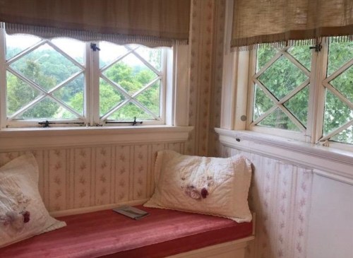 Cozy window nook with a pink cushion, floral pillows, and scenic views of greenery outside.