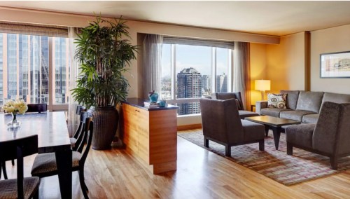 A modern living room with large windows, a dining table, and stylish furniture, offering a city view.