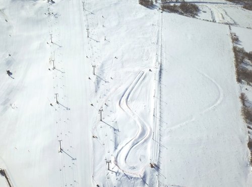 Aerial view of a snowy ski slope with winding tracks and ski lifts in the background.
