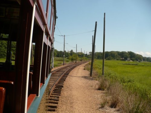 A view from a train window showing a winding railway track through a grassy landscape under a clear blue sky.