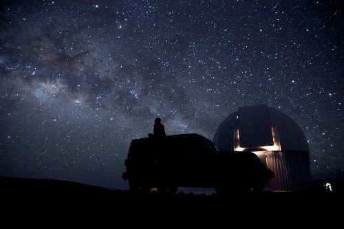 A silhouette of a person on a vehicle, gazing at a starry sky above an observatory dome.