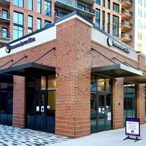 Exterior of a brick building with large glass doors, featuring a sign for "Insomnia Cookies" and an open sign.
