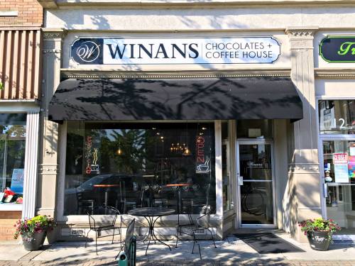 Exterior of Winans Chocolates + Coffee House, featuring a black awning and outdoor seating, with an "Open" sign in the window.