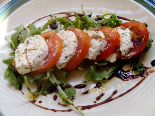 A plate of sliced tomatoes and creamy cheese on a bed of arugula, drizzled with balsamic glaze.