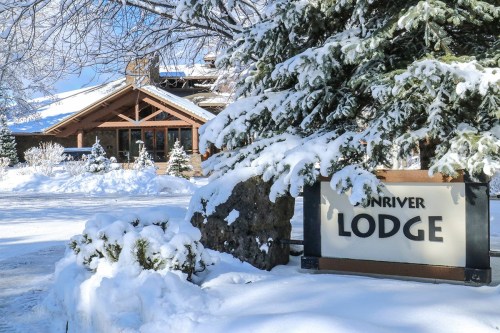 A snowy landscape featuring a lodge sign surrounded by evergreen trees and a wintery scene.