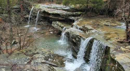 A serene landscape featuring a small waterfall cascading over rocky terrain into a calm pool of water.