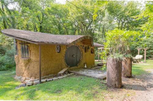 A whimsical, round cottage with a thatched roof, surrounded by greenery and rustic wooden features.