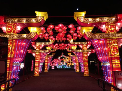 Colorful lanterns and illuminated arches create a festive atmosphere at night, with a crescent moon in the sky.