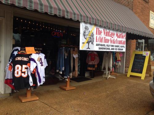 A storefront with a striped awning, displaying vintage clothing and a sign for antiques, gifts, and ice cream.