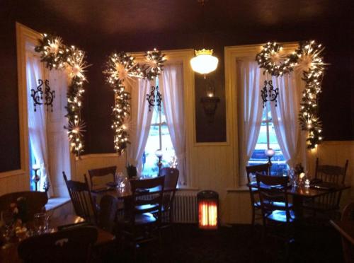 Cozy restaurant interior decorated with festive lights and greenery, featuring wooden tables and chairs.