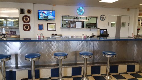 A retro diner interior featuring a blue and silver counter with stools, a TV, and a mirrored wall.