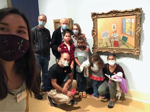A group of people wearing masks poses in front of a painting in an art gallery.