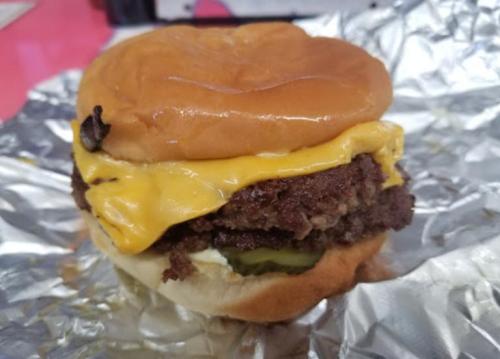 A juicy cheeseburger with two beef patties, melted cheese, pickles, and a soft bun, wrapped in foil.