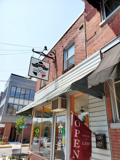 A brick storefront with an "OPEN" sign and a hanging shop sign, located on a sunny street in Lititz.