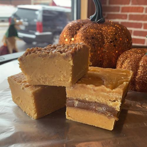 Three layers of fudge stacked on a surface, with decorative pumpkins in the background.