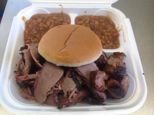 A takeout container with sliced brisket, a bun, and baked beans.
