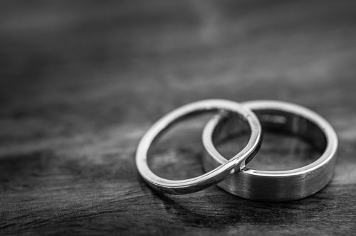 Two silver wedding rings intertwined on a wooden surface, captured in black and white.