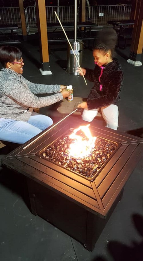 Two people enjoying a fire pit outdoors, one roasting marshmallows while the other holds a drink.